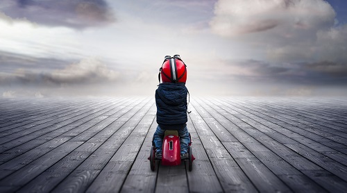 Ein Kind auf einem roten Spielauto auf einem Holzboden welcher bis zum Horizont führt, Quelle: © Shutter81/Stock Adobe
